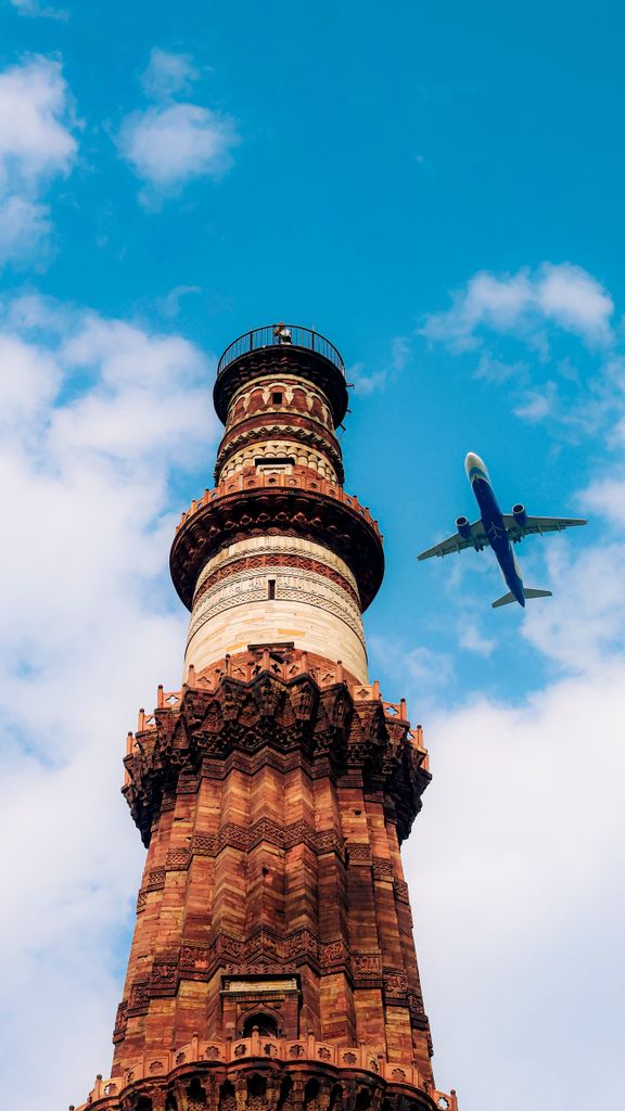 A dramatic view of Qutub Minar with an airplane flying in a clear blue sky.