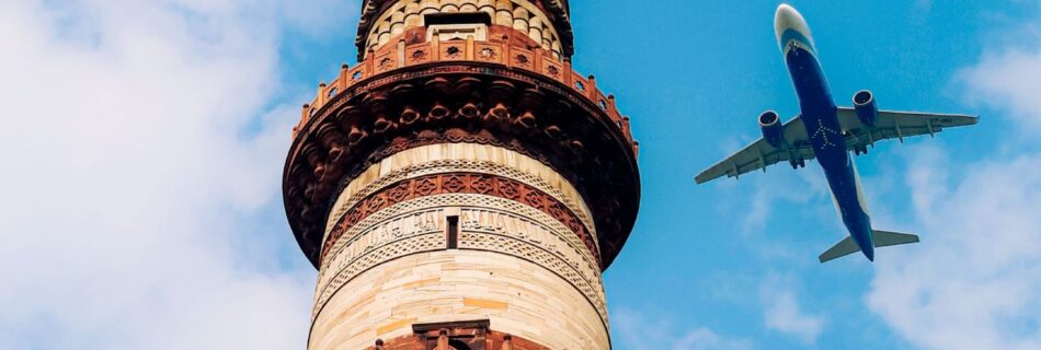 A dramatic view of Qutub Minar with an airplane flying in a clear blue sky.