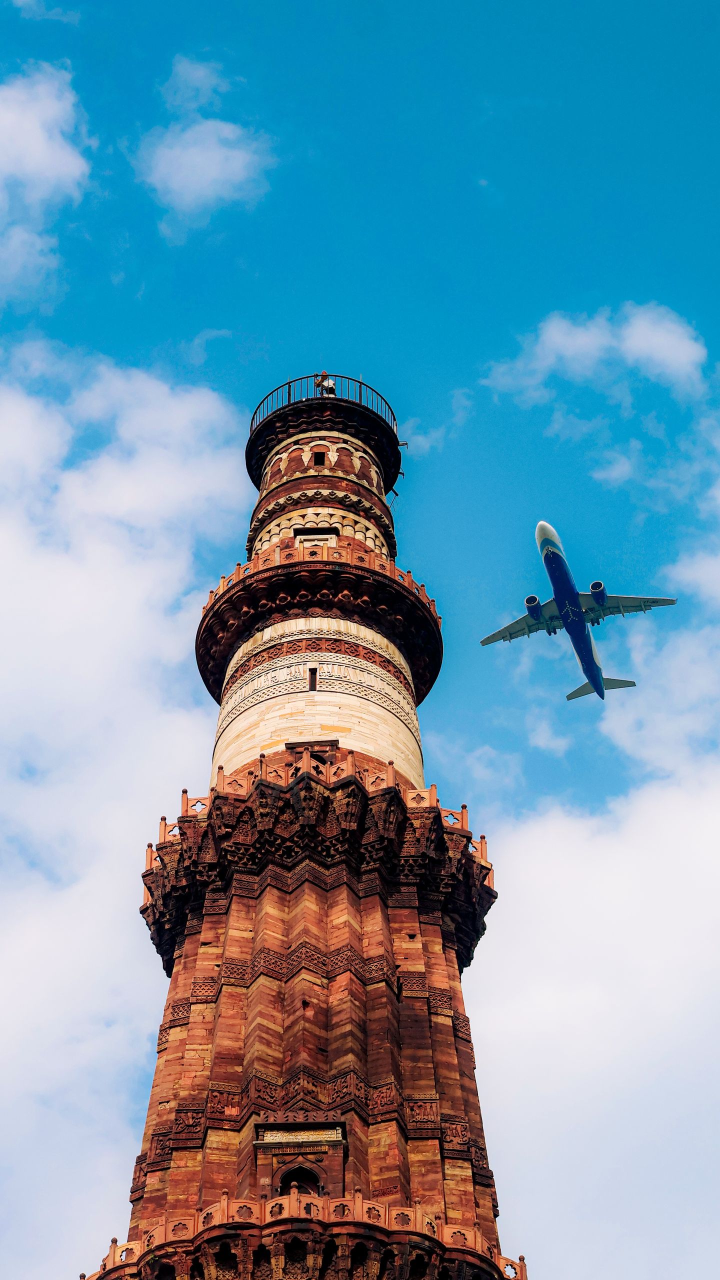 A dramatic view of Qutub Minar with an airplane flying in a clear blue sky.