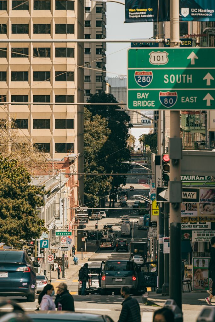 Busy downtown street scene with cars, pedestrians, and signs under sunny skies.