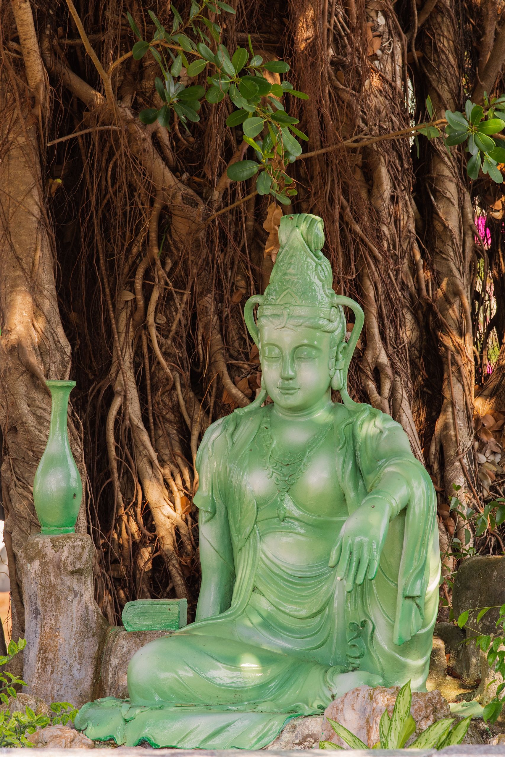 Green Buddha statue in a serene outdoor setting against a large tree.