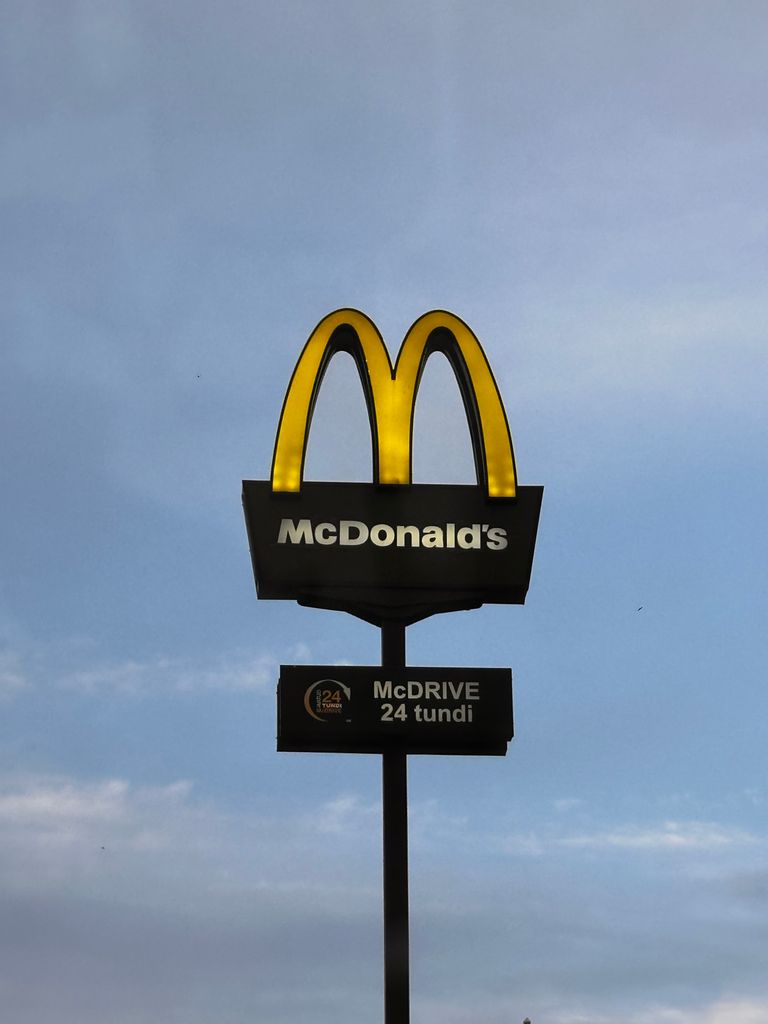 McDonald's sign with a golden arch under a clear blue sky, promoting 24-hour drive-thru.
